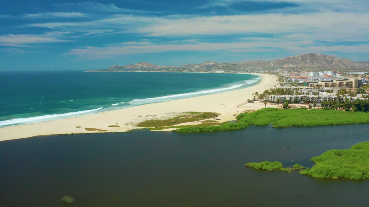 Aerial view of lagoon, beach, ocean waves, and distant hills