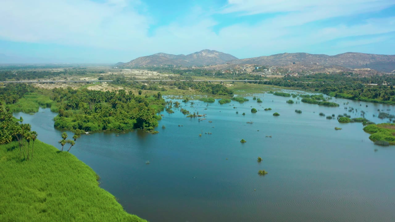 Aerial view in San Jose del Cabo with open water in the foreground, scattered green islands across the middle, low hills on the horizon, and no visible people.