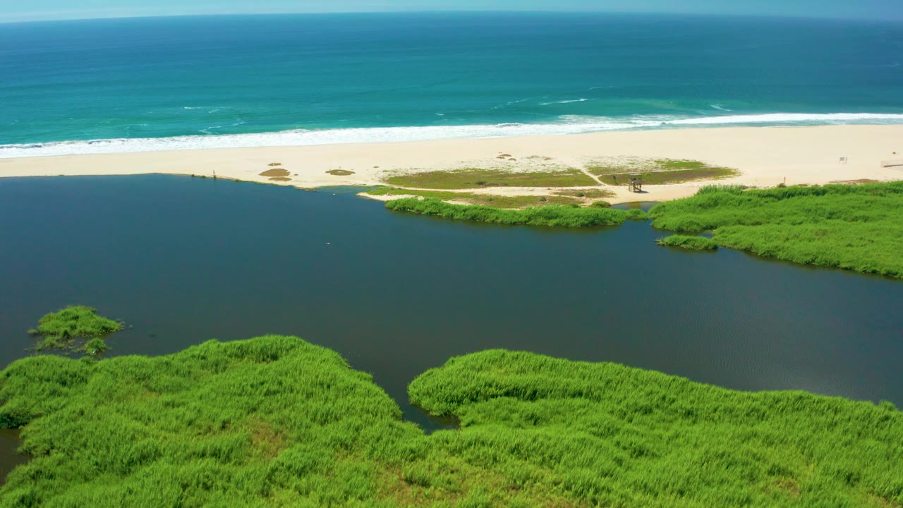 Aerial shot of a coastal lagoon bordered by mangroves and a wide sandy beach.