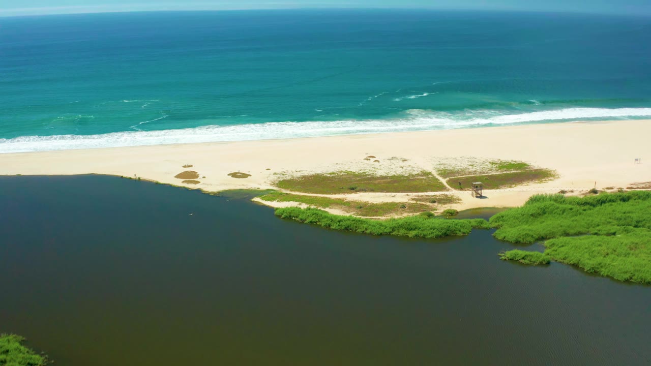San Jose del Cabo coastline from above, with the estuary filling the lower frame, a narrow sandy beach across the center, white waves offshore, and no visible people.