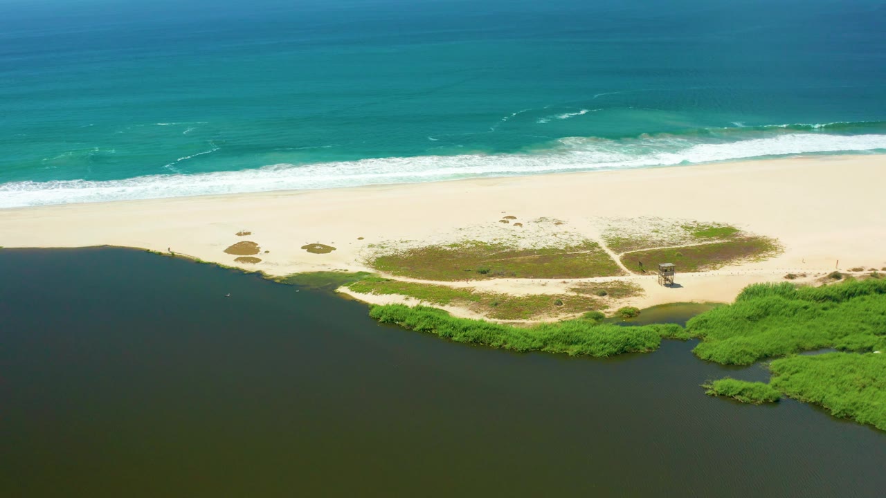 Aerial frame of a beach path, estuary mouth, and ocean waves.