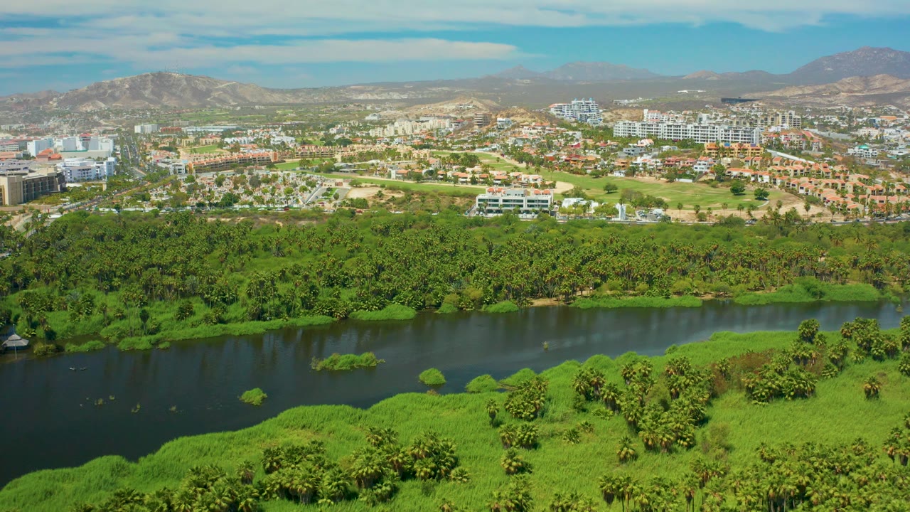 Aerial view across dark water, green trees, buildings, and mountain ridge.