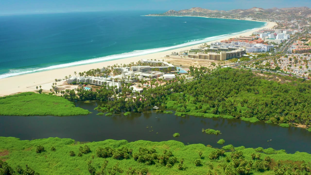 Aerial coastline with lagoon water in front, beach and buildings in the middle, and ocean beyond.