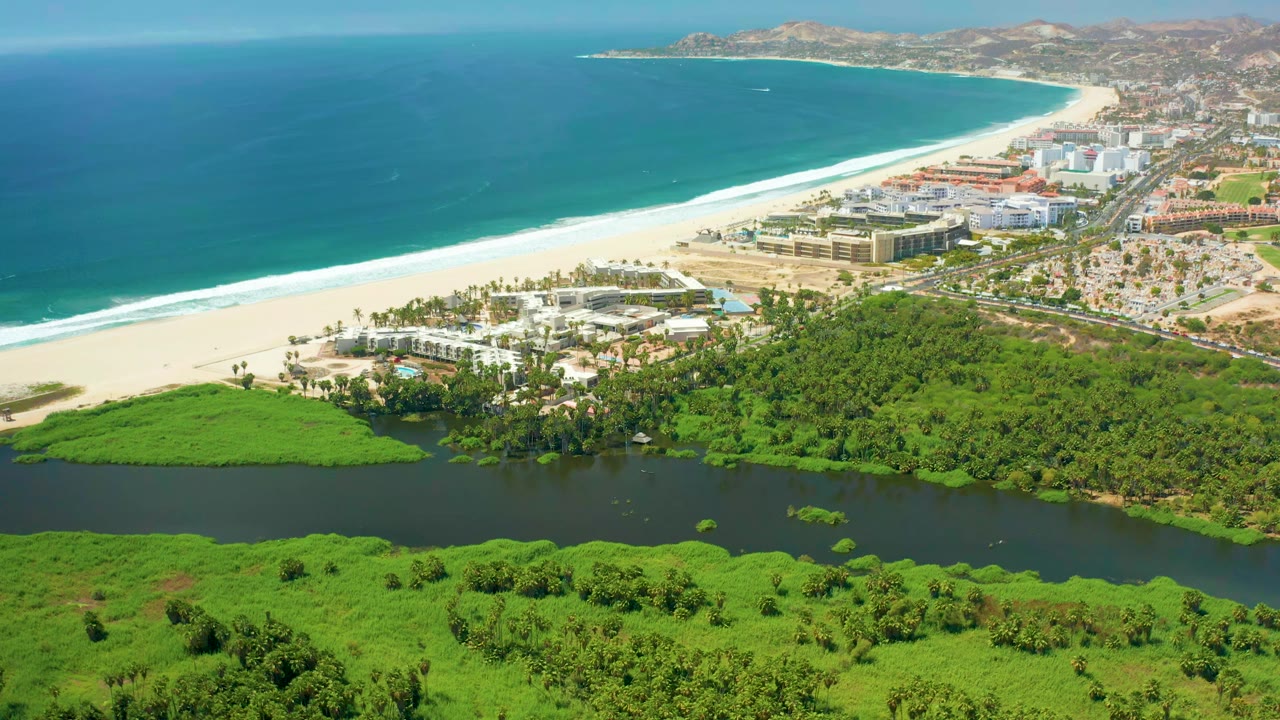 Aerial coastline with lagoon foreground, beach, ocean, buildings, and hills.