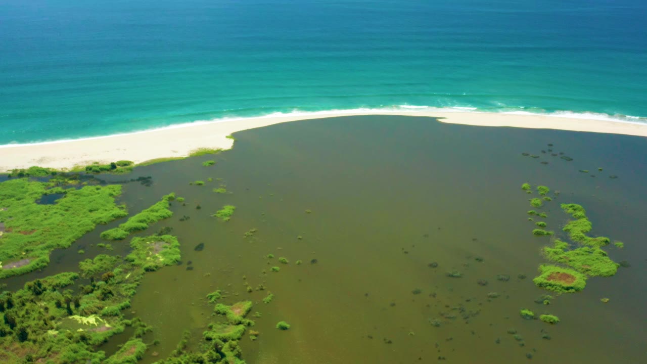 Aerial view of green lagoon, mangroves, sand beach, and turquoise ocean.