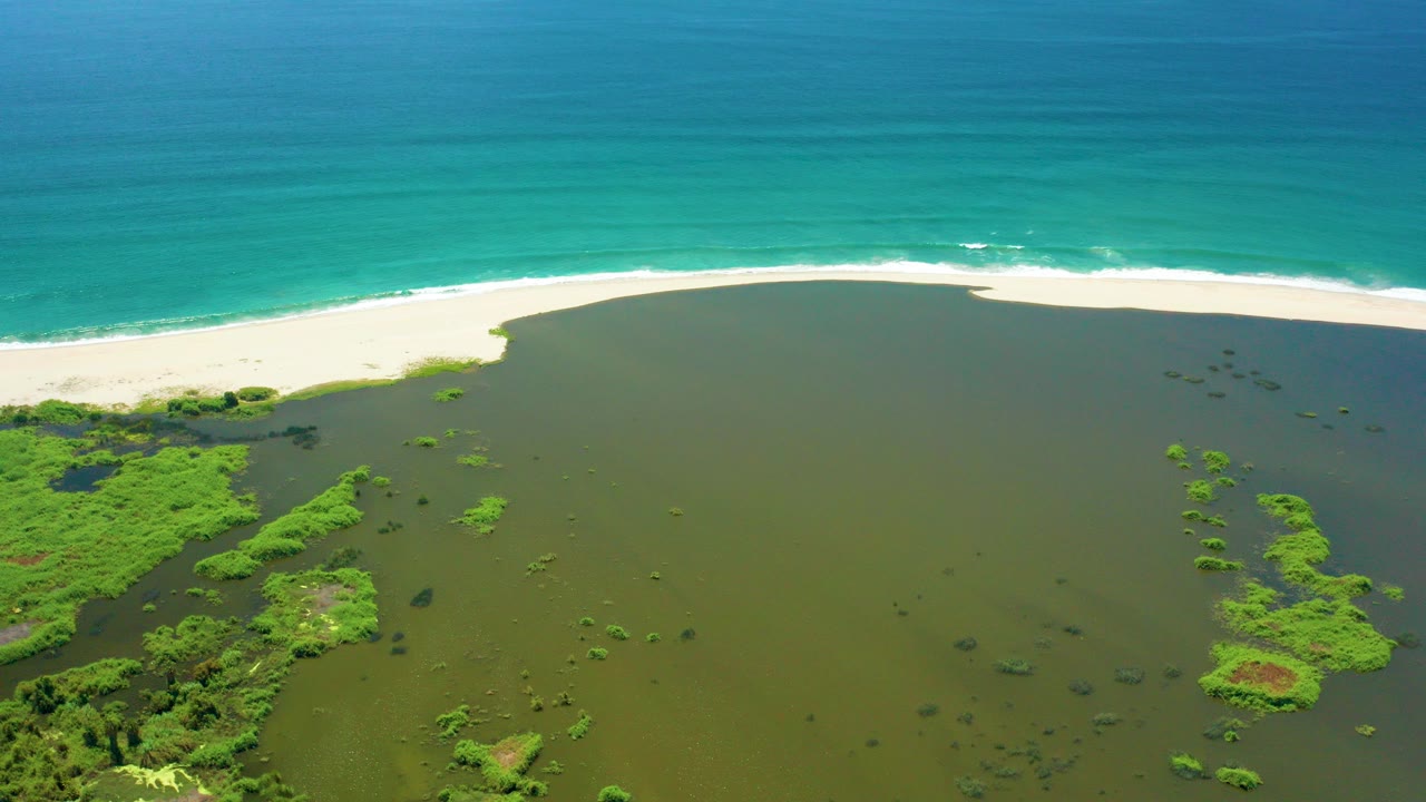 Aerial frame from San Jose del Cabo showing green lagoon water below a white sand beach and turquoise ocean beyond, with no visible people.