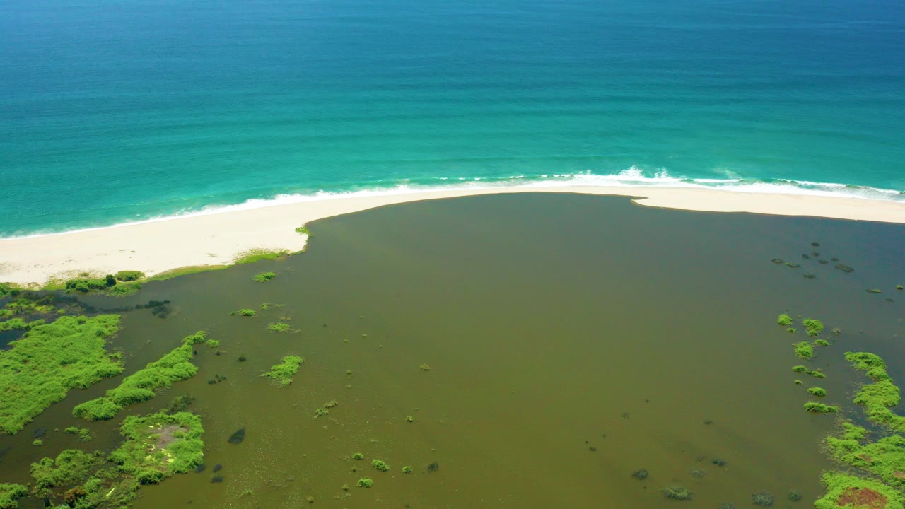 Aerial view of green lagoon, white sand beach, and turquoise ocean surf.