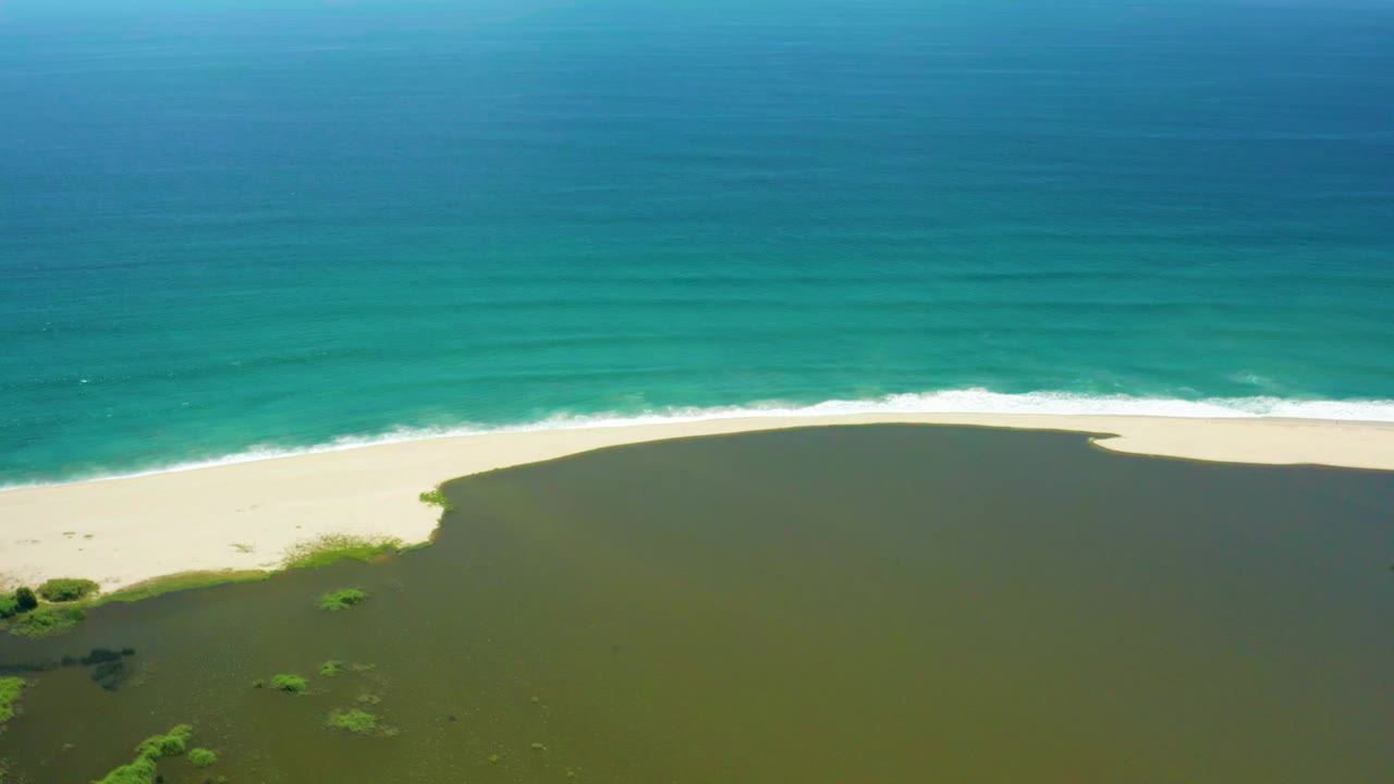 Aerial view of a sandy beach between green lagoon water and turquoise ocean.