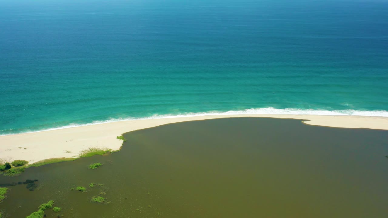 San Jose del Cabo aerial frame showing a broad turquoise ocean band above a pale beach and green lagoon, with no visible people or built structures.