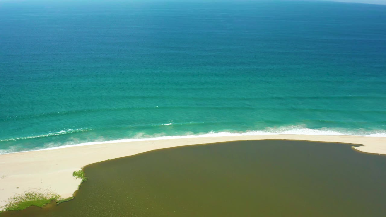 A San Jose del Cabo aerial view shows the surf line slightly farther across the sand, with blue-green ocean above and the lagoon curving below, no visible people.