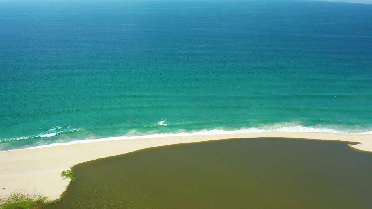 Ocean waves approach a sandy beach with a green lagoon in the foreground.