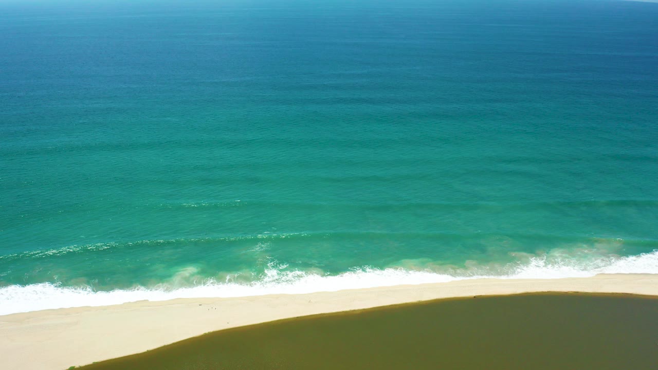 Turquoise ocean waves breaking onto a pale sandy shore.