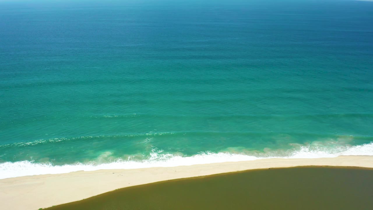 Aerial frame in San Jose del Cabo showing white foam spreading along the beach as turquoise water fills most of the view, with no visible people.