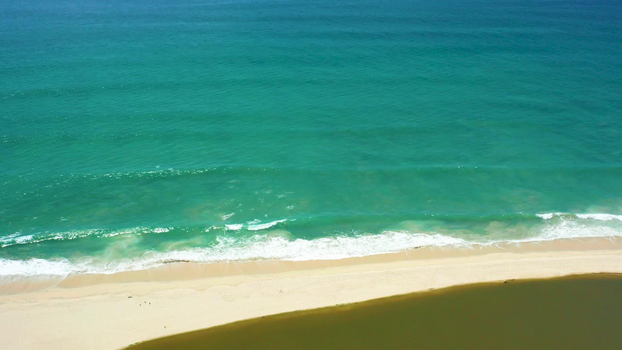 Turquoise ocean waves reaching a sandy beach from above