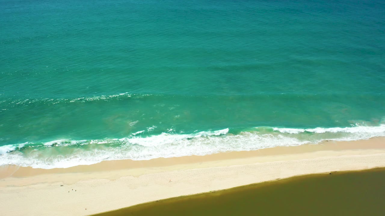 San Jose Del Cabo beach seen from above with smooth turquoise water, small whitecaps near shore, pale sand below, and no visible people.