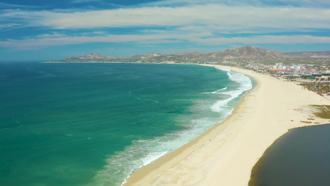 Aerial coastal view with white surf curling onto an empty sandy beach.