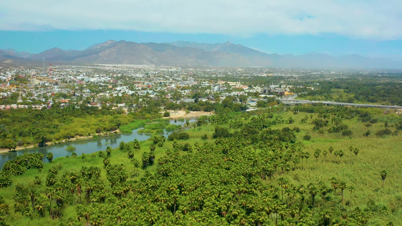 Aerial landscape with river water, trees, town buildings, and distant mountains.