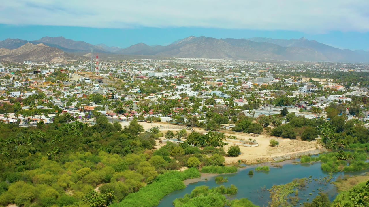 Wide aerial cityscape with river vegetation and mountain horizon.
