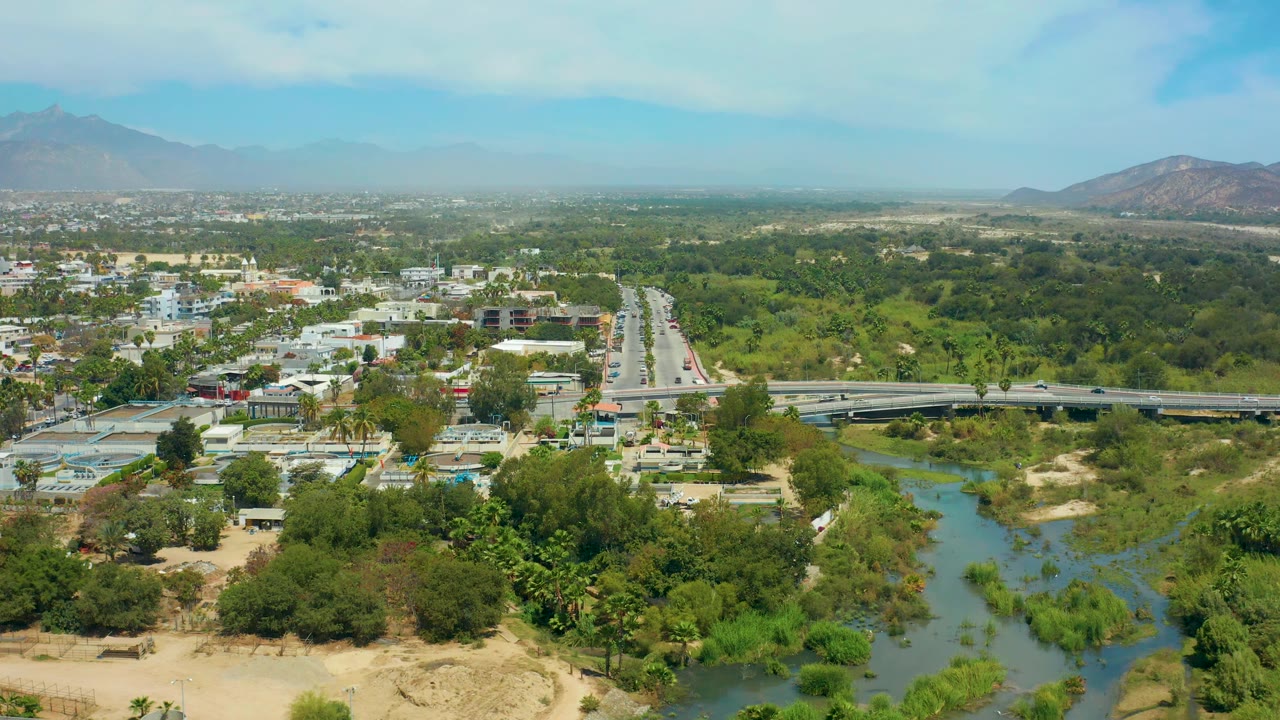Aerial landscape with river foreground, bridge, roadway, buildings, trees, and mountains.