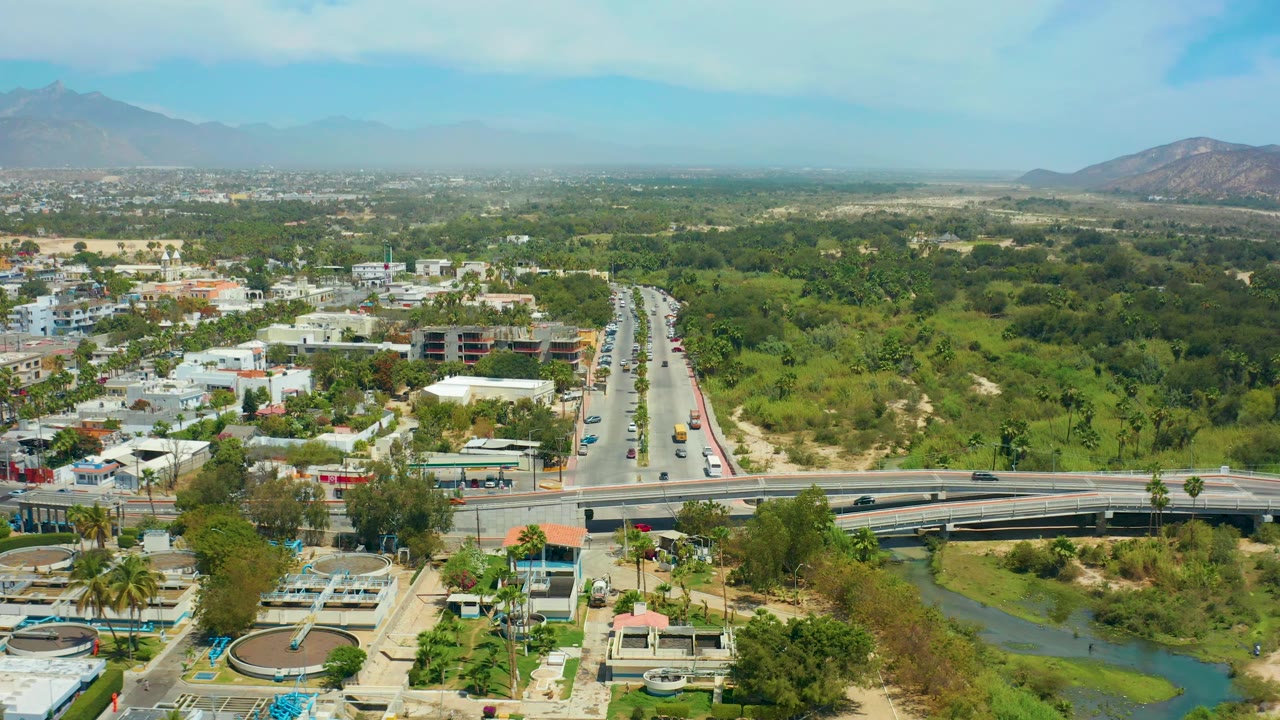Aerial view of bridge and highway beside buildings and a green river channel.