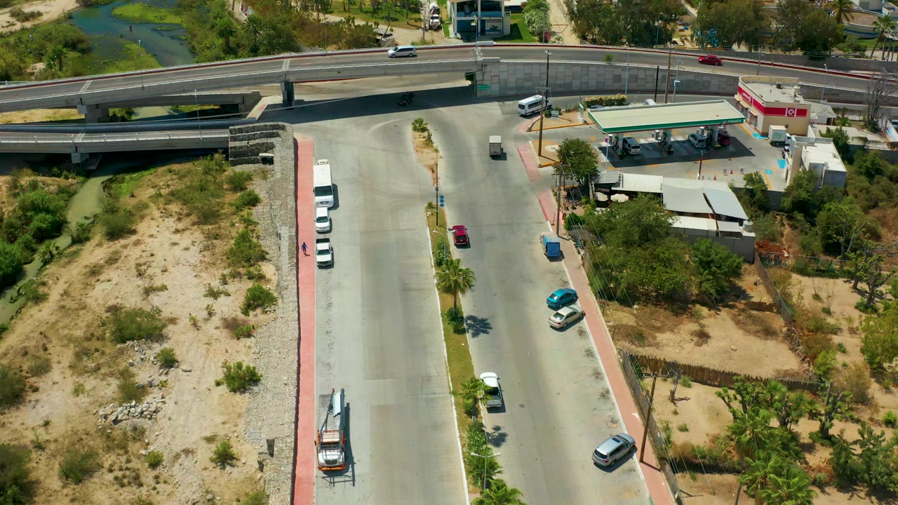 Vehicles move near an overpass with a gas station and dry roadside lots nearby.