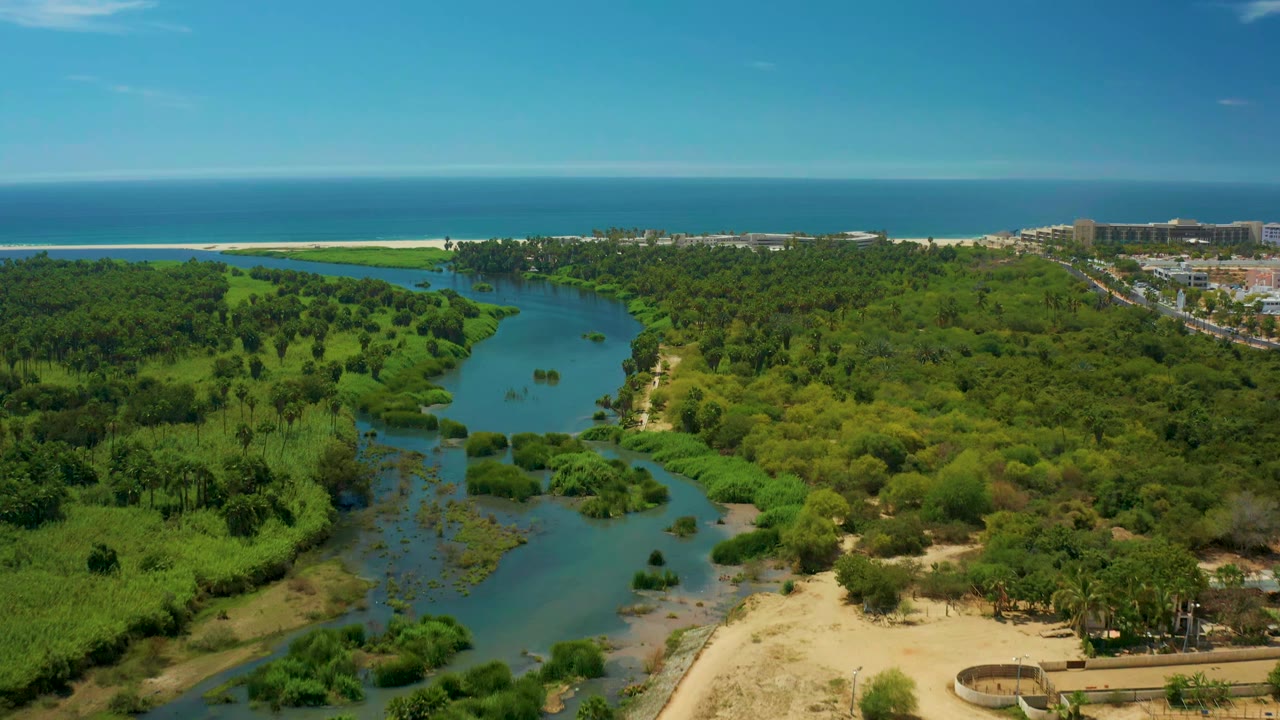 Wide aerial view of blue river water crossing green vegetation near a beach and ocean.