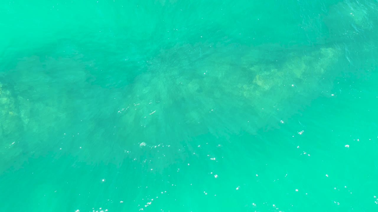 Clear green-blue water at Marquis Los Cabos shows the seabed slightly softened by surface shimmer, with a few bright bubbles and no visible people.