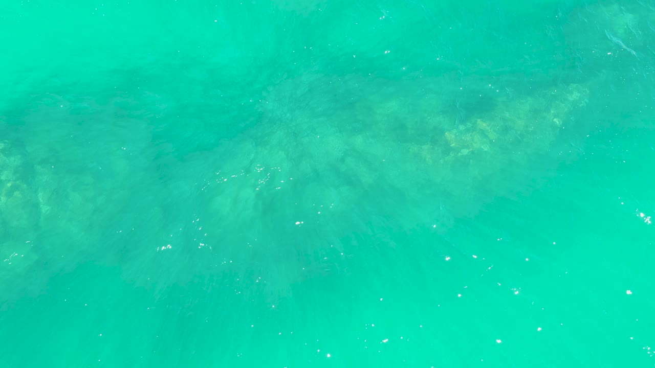 Bright turquoise water at Marquis Los Cabos reveals darker rock patches below, light specks on the surface, and no visible people.