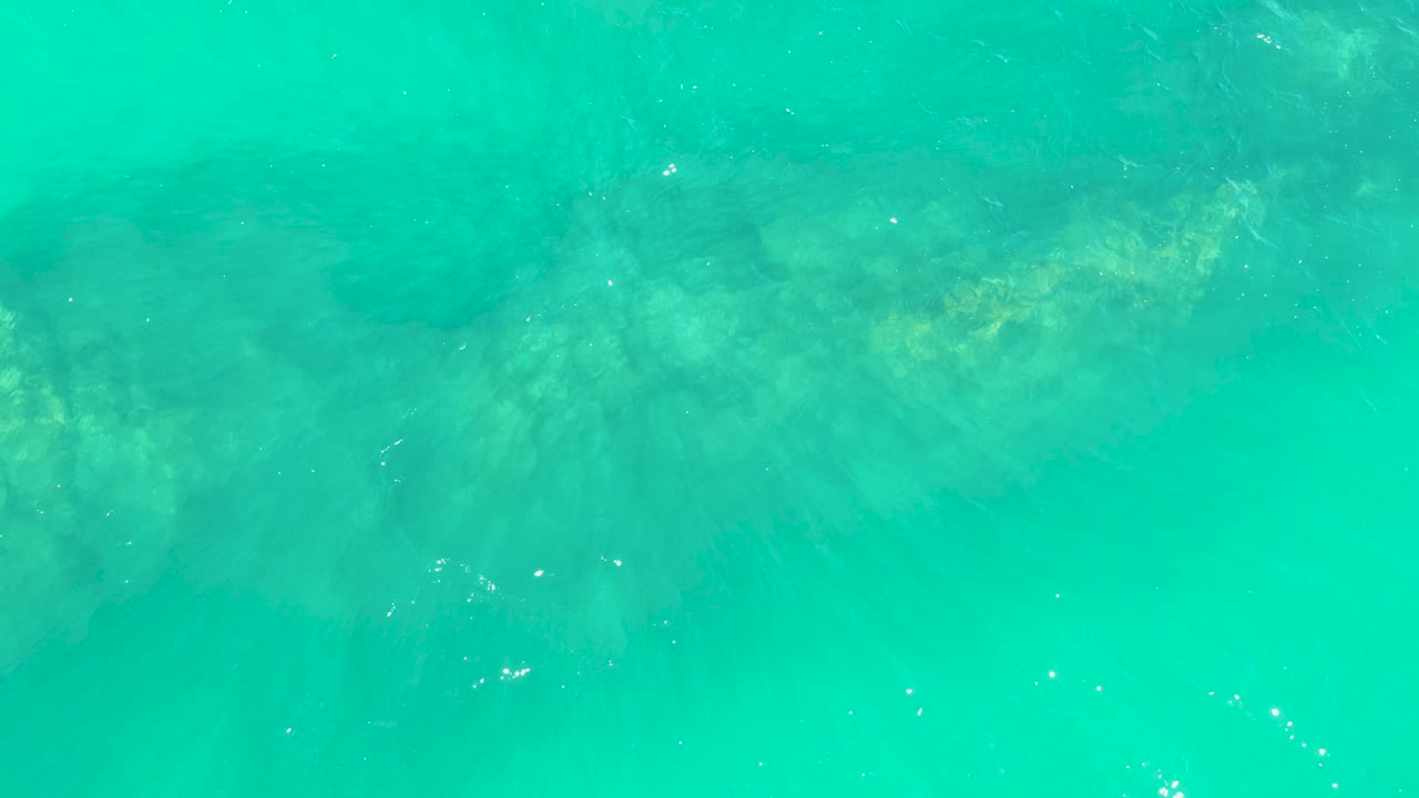Clear turquoise water covers soft submerged rock shadows at Marquis Los Cabos, with tiny white specks near the surface and no visible people.