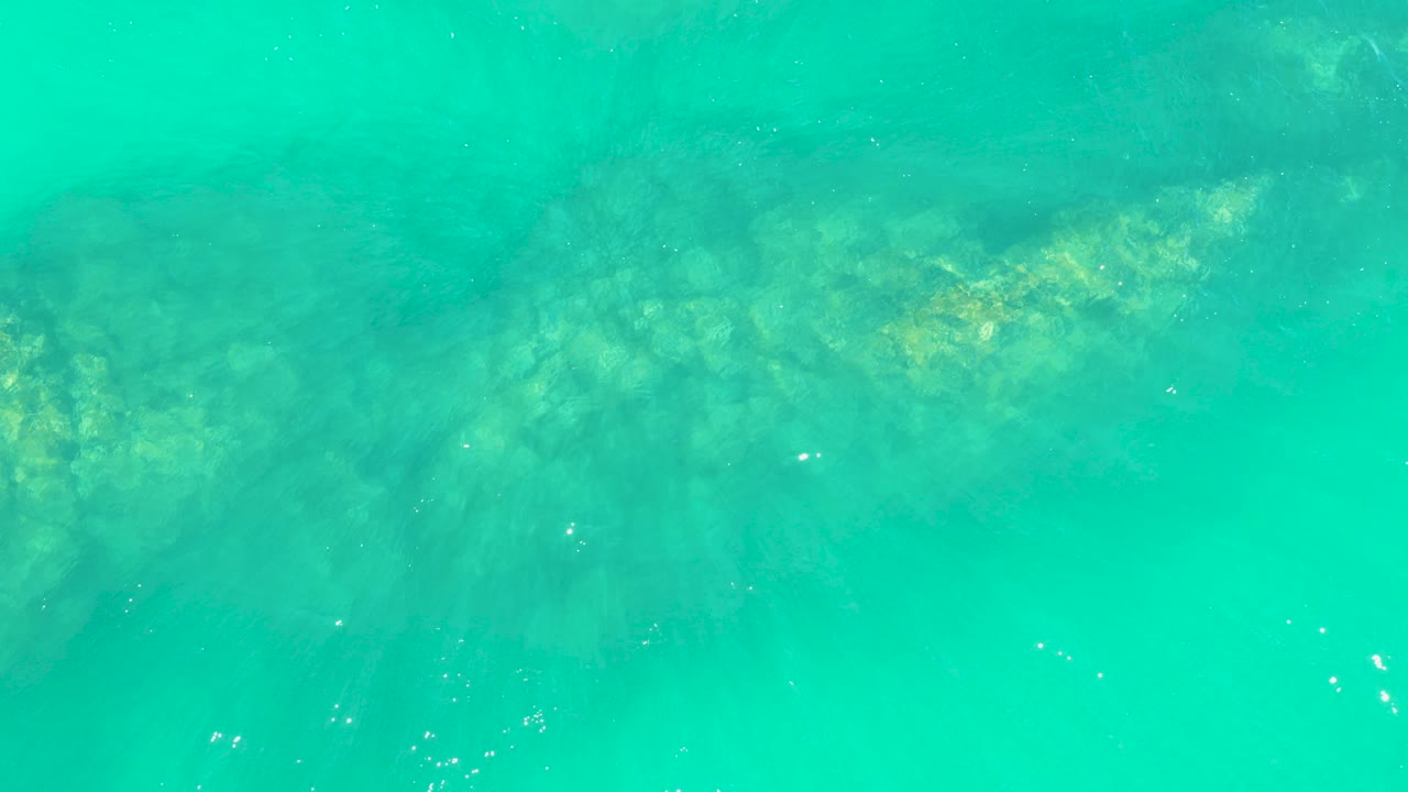 Overhead view of turquoise water at Marquis Los Cabos with a submerged reef shape faintly visible near the upper half and no visible people.