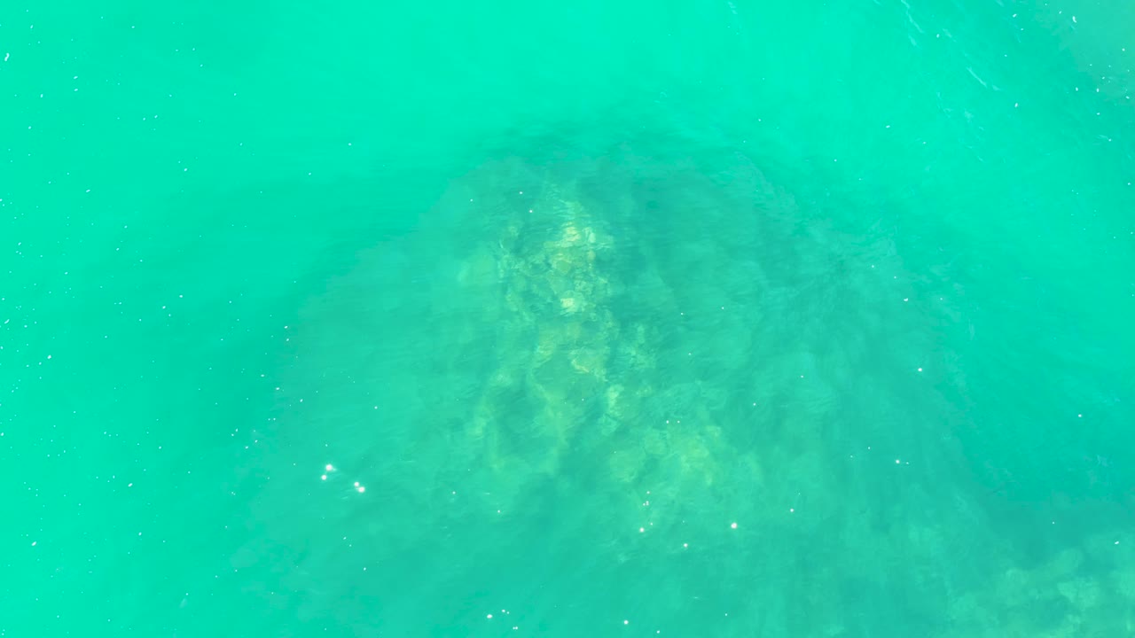 The underwater rock at Marquis Los Cabos sits slightly right of center under blue-green water, showing brighter yellow-green patches and no visible people.