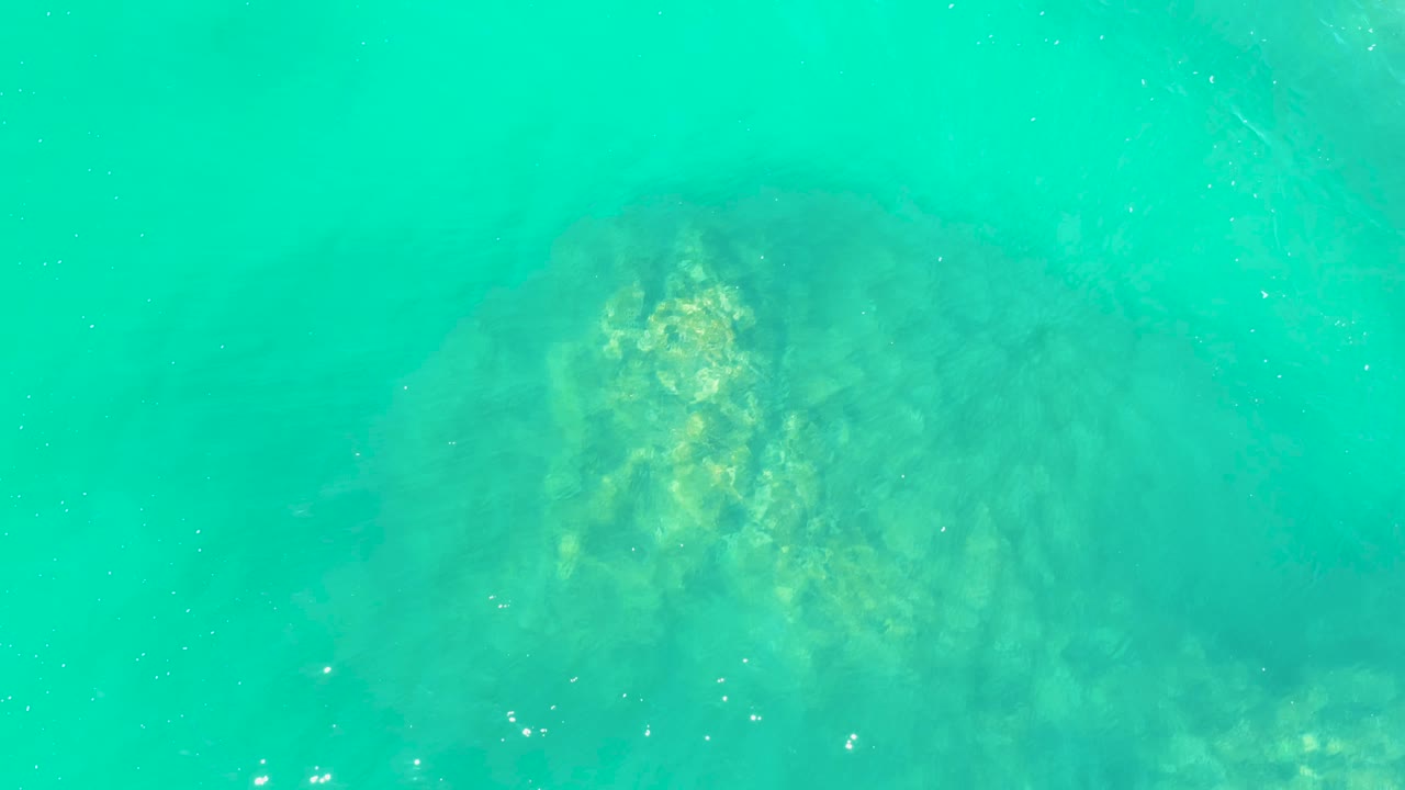 A brighter patch of submerged rock appears through rippled turquoise water at Marquis Los Cabos, with no visible people.