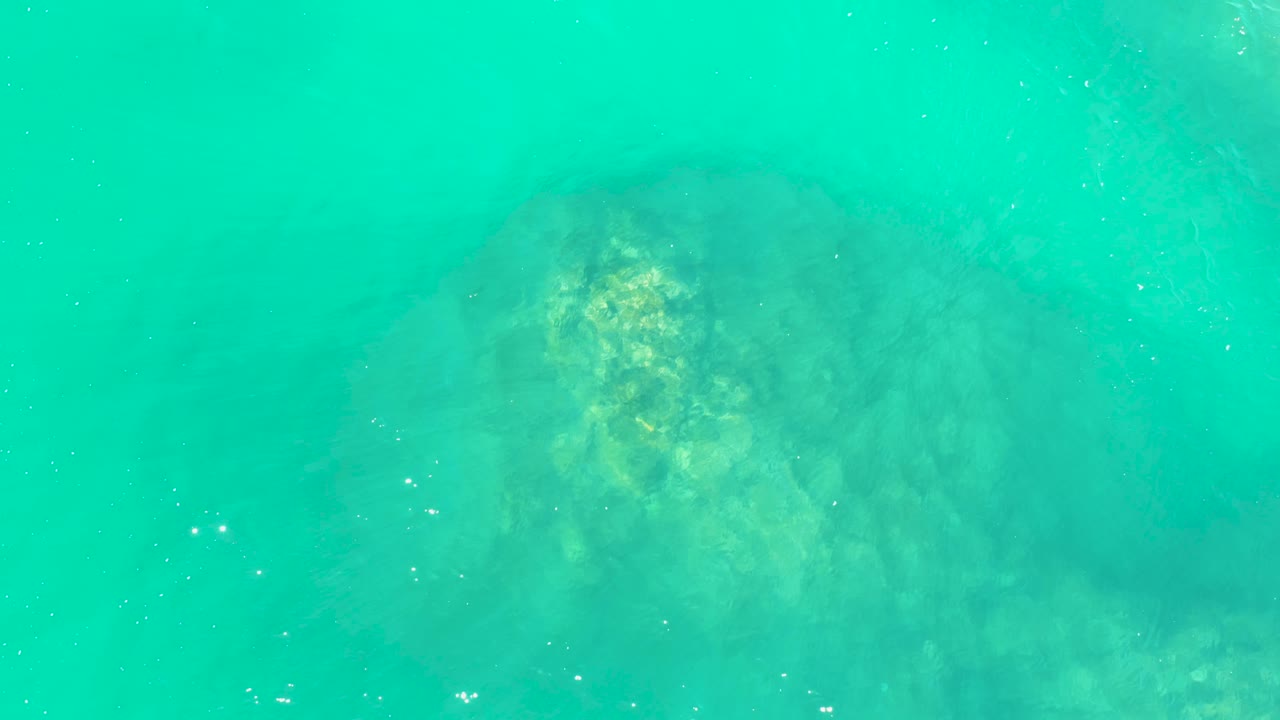 The submerged rock remains near the upper center under turquoise water at Marquis Los Cabos, softened by surface movement and with no visible people.