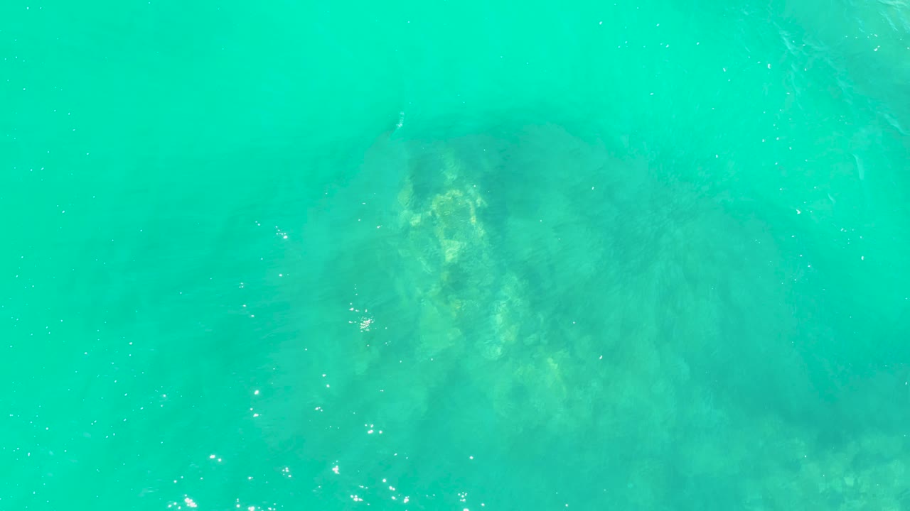 A muted submerged rock sits below clear turquoise water at Marquis Los Cabos, with small glints near the surface and no visible people.