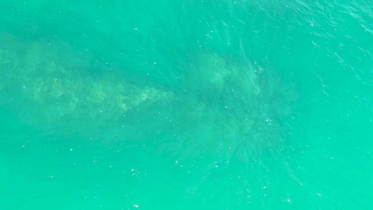 Overhead view of clear turquoise water at Marquis Los Cabos with a pale submerged structure faintly visible below the rippled surface and no visible people.
