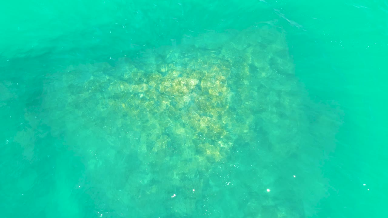 Sunlit rocks appear through shallow turquoise water at Marquis Los Cabos, with brighter rippled highlights across the seabed and no visible people.