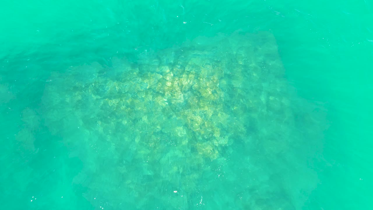 The underwater view at Marquis Los Cabos shows the rocky seabed slightly softened by water haze, with pale specks in the water and no visible people.