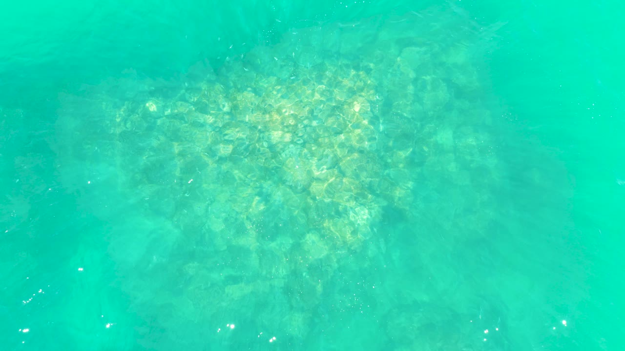 Overhead view of clear turquoise water over a rocky seabed at Marquis Los Cabos, with soft sunlit patches and no visible people.