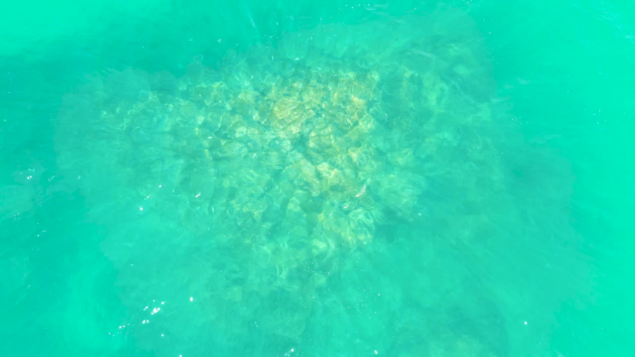 A pale rocky seabed sits beneath turquoise water at Marquis Los Cabos, with the brightest rock cluster near the upper center and no visible people.