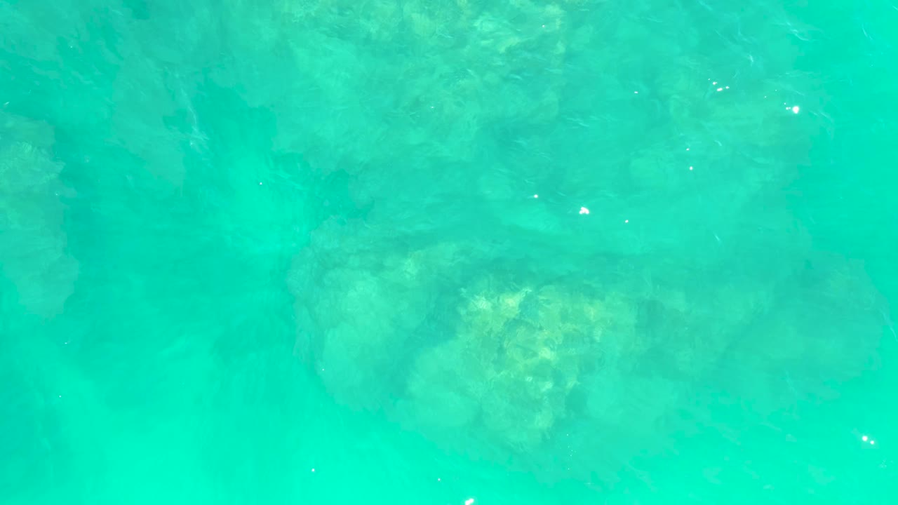 Turquoise water at Marquis Los Cabos with a rocky seabed visible through the center of the frame and faint ripples across the surface, no visible people.