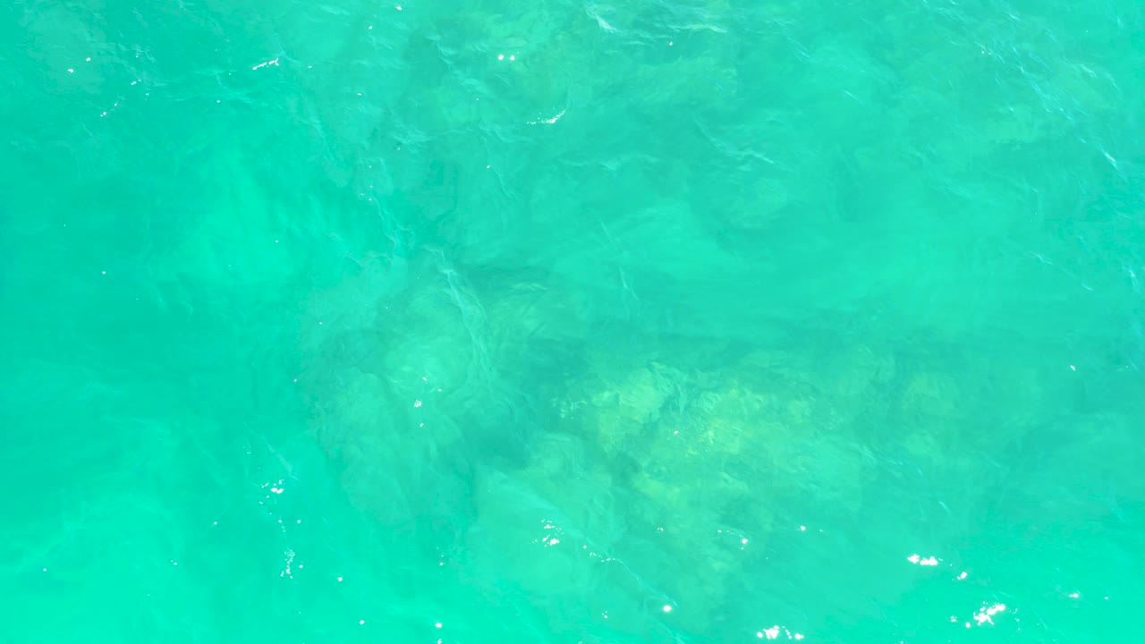 Turquoise ocean water at Marquis Los Cabos shows faint submerged rock forms under a lightly rippled surface, with no visible people.