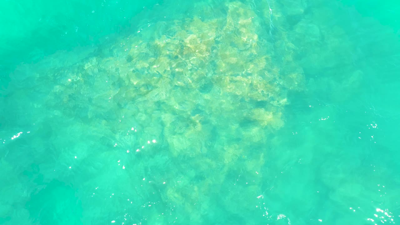 Clear green-blue water reveals a clustered rocky seabed at Marquis Los Cabos, with ripples slightly softening the rock outlines and no visible people.