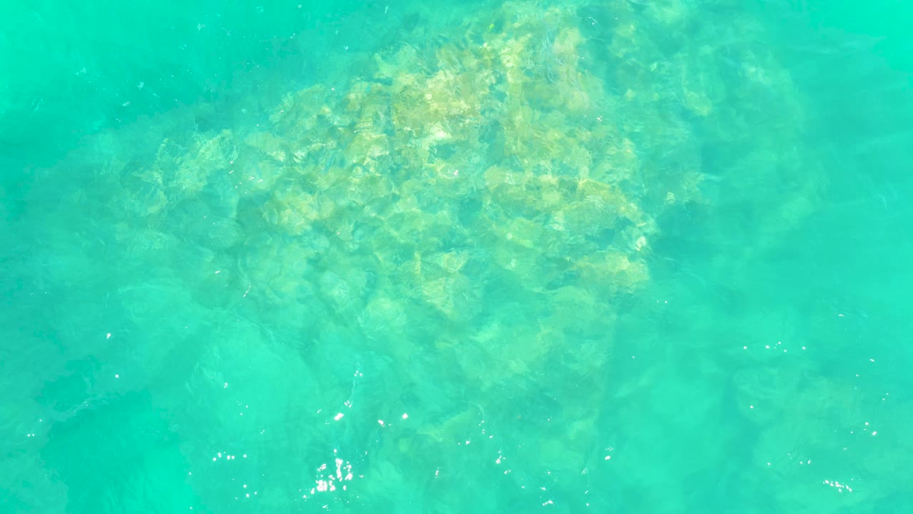 Shallow turquoise ocean water at Marquis Los Cabos shows submerged rocks near the left side of frame, with wavering light and no visible people.