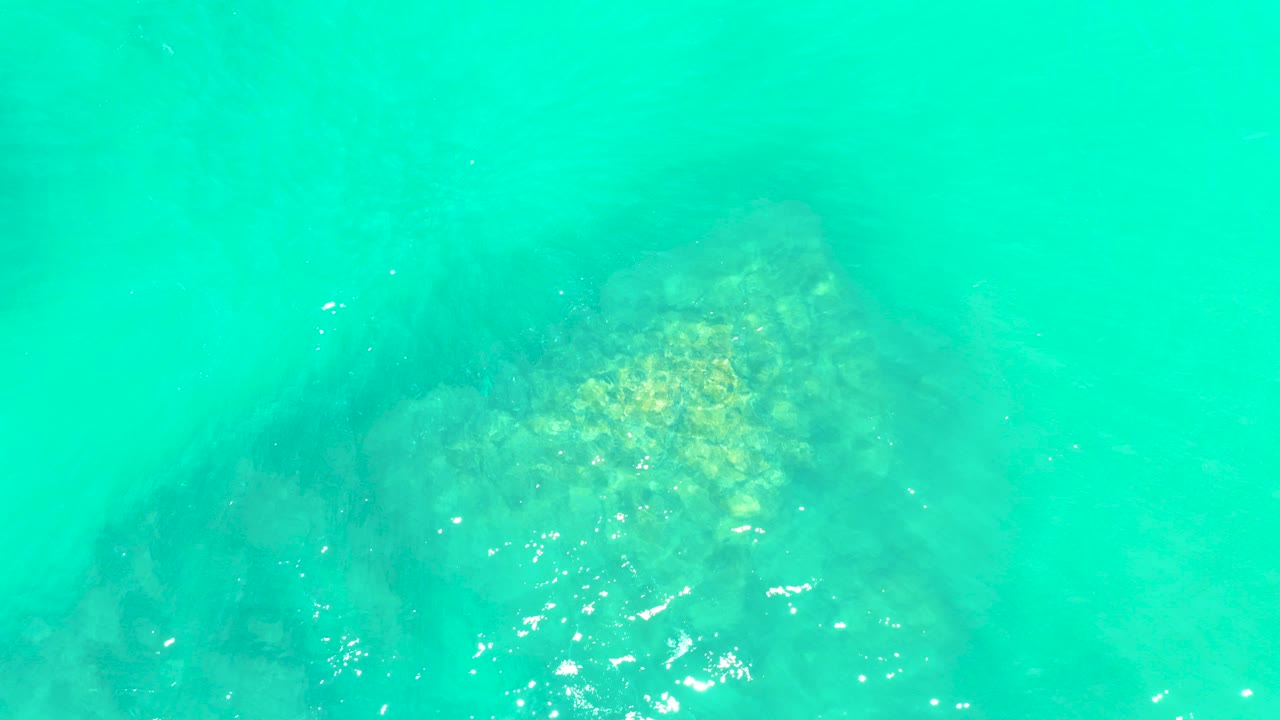 Clear turquoise water at Marquis Los Cabos shows a submerged rock formation beneath bright surface reflections, with no visible people.