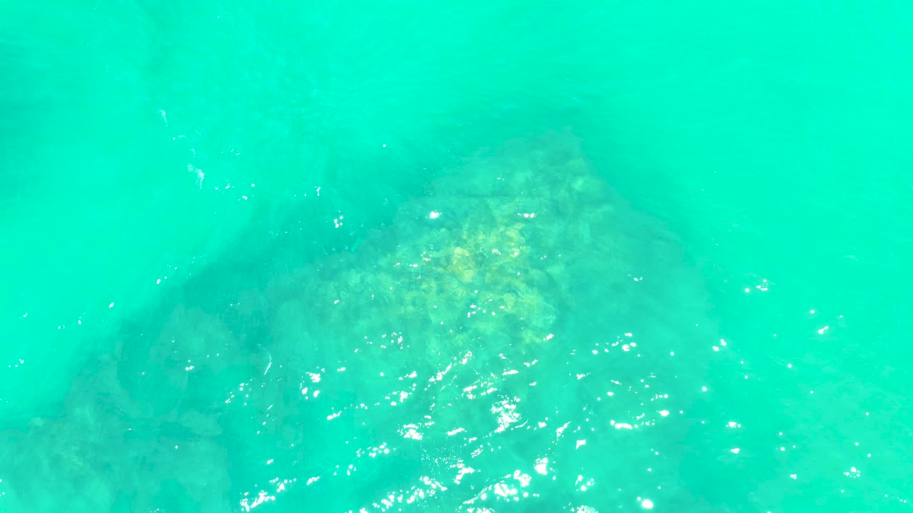 Transparent turquoise sea at Marquis Los Cabos reveals the darker outline of a submerged rock beneath scattered highlights, with no visible people.