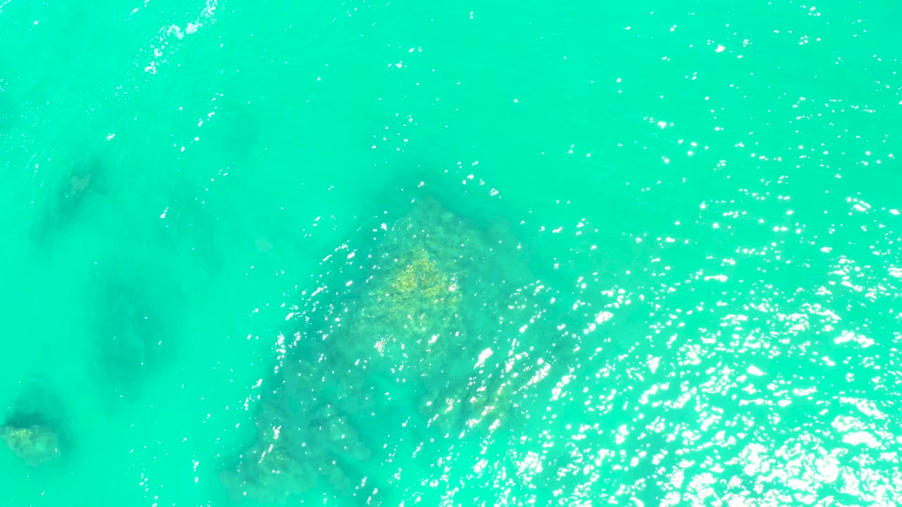 Clear turquoise water with underwater rocks near the left side and sparkling ripples