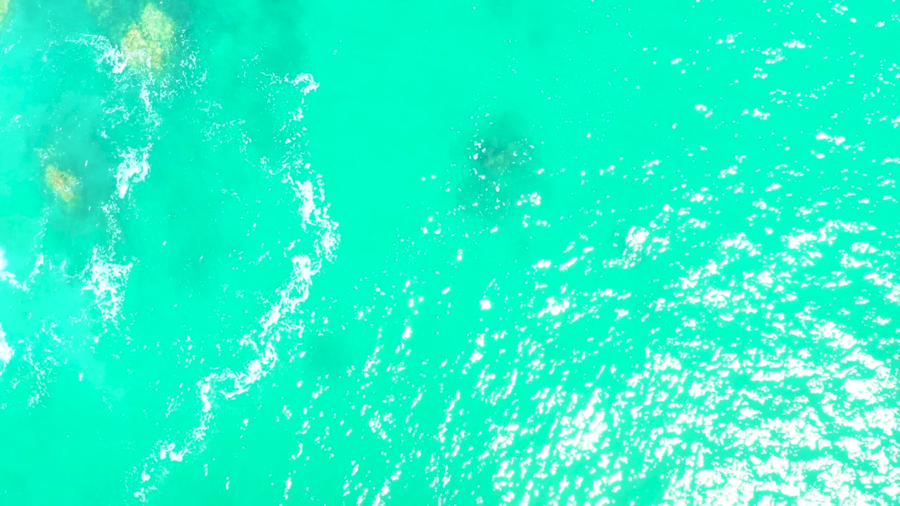 Clear turquoise water with rocks at the left and white foam.
