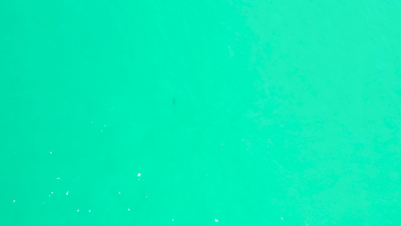 Top-down view of turquoise sea at Marquis Los Cabos with pale foam specks, faint darker water patches, and no visible people.