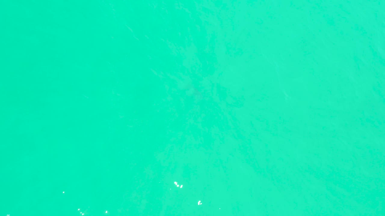 Clear turquoise water fills the frame at Marquis Los Cabos, with faint seabed variation and tiny bright white marks visible against the water, no visible people.