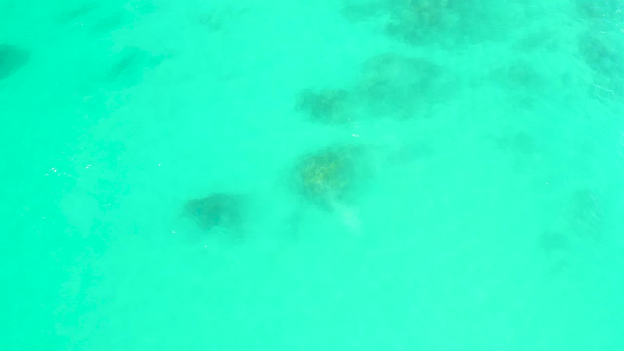 Turquoise ocean water at Marquis Los Cabos shows several darker reef-like rock patches softened by ripples, no visible people.